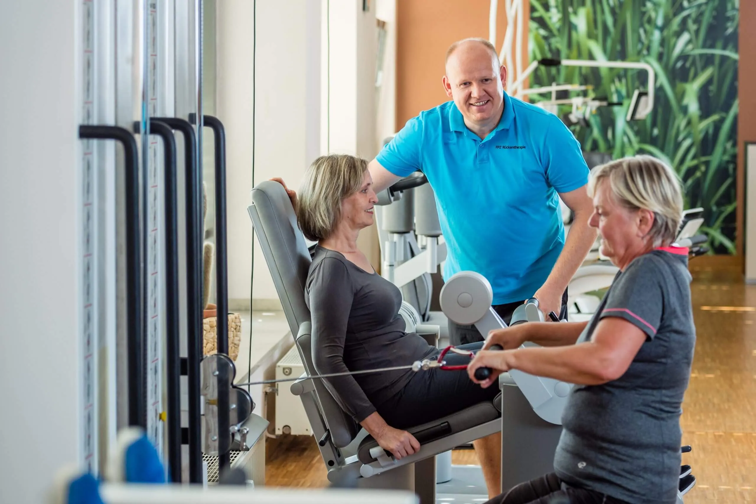 Therapeut betreut zwei Patientinnen an Trainingsgeräten