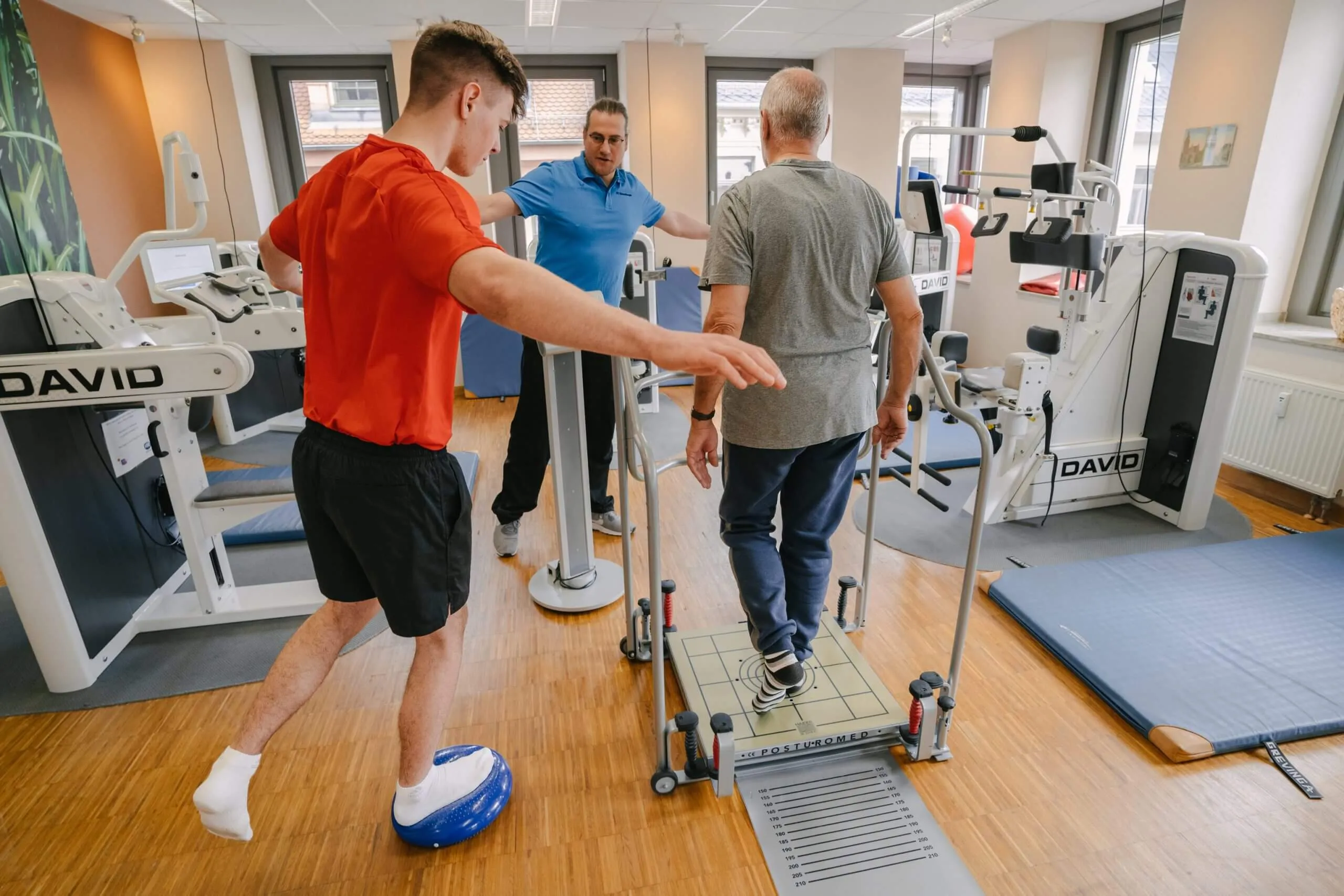 Zwei Therapeuten leiten einen Patienten an einem Trainingsgerät an